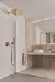 Elegante Dusche mit runder Regenbrause in Brushed Gold, montiert an der Decke, kombiniert mit einem Wandarmaturenset von Ideal Standard in einem modernen Badezimmer.